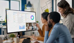 Employees gathered around a screen using team collaboration tools with a shared dashboard in a modern office setting