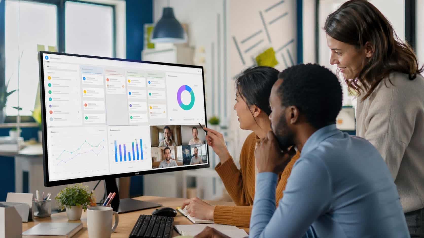 Employees gathered around a screen using team collaboration tools with a shared dashboard in a modern office setting
